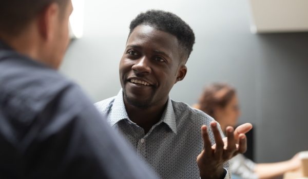 African american businessman professional manager talking to male caucasian colleague client discussing work project having friendly business conversation consulting customer teach intern in office