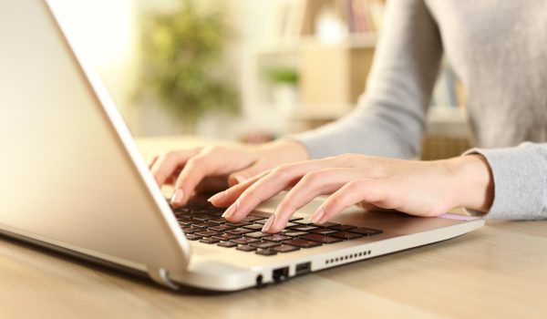 Close up of woman hands typing on laptop sitting on a desk at home