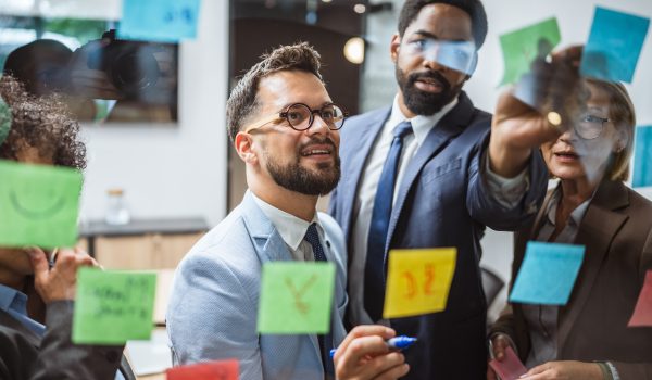 Multicultural business professionals man and woman coworkers brainstorming and planning, work on new project use sticky notes on glass wall in the office